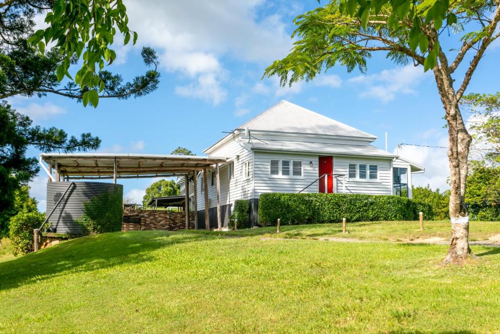 ein weißes Haus mit einer roten Tür und einem Baum in der Unterkunft Thirlestane Farm Cottage & Barn in Cooroy