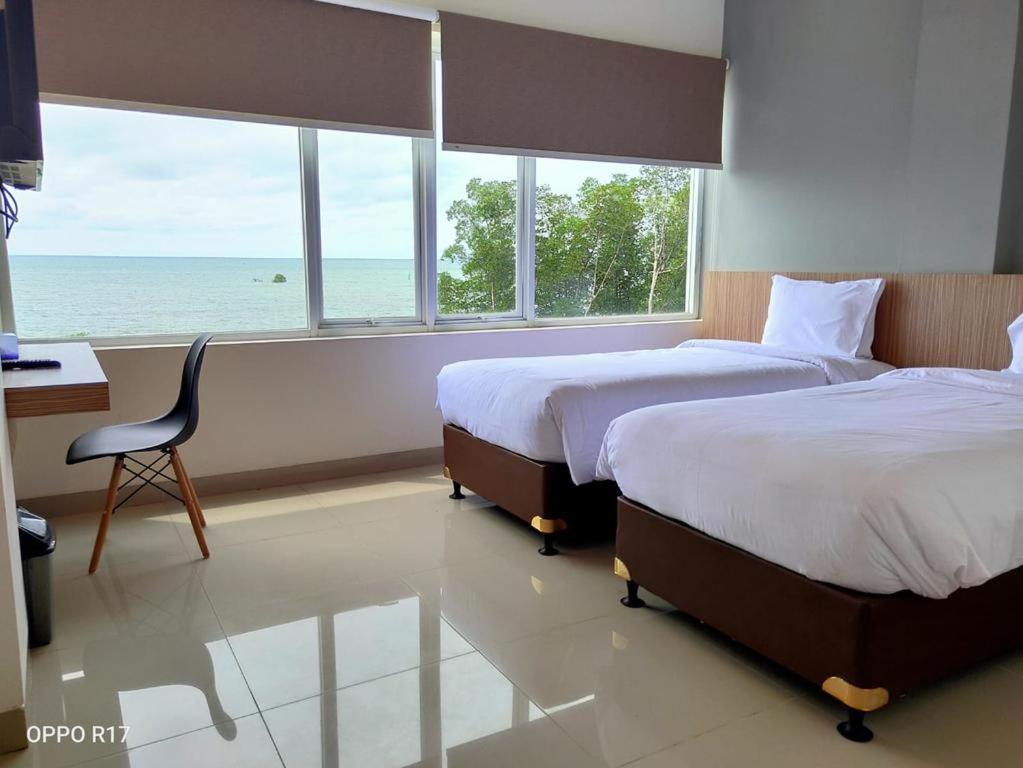 a bedroom with two beds and a desk and a window at The Holiday Guest House in Tanjungpandan