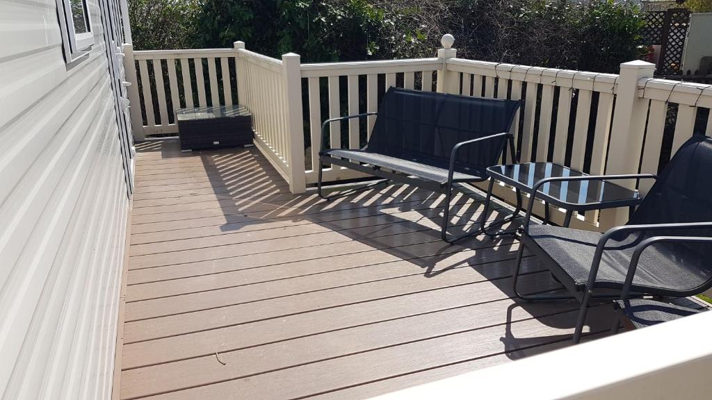 2 sillas y un banco en una terraza de madera en The Summers residence, en Selsey