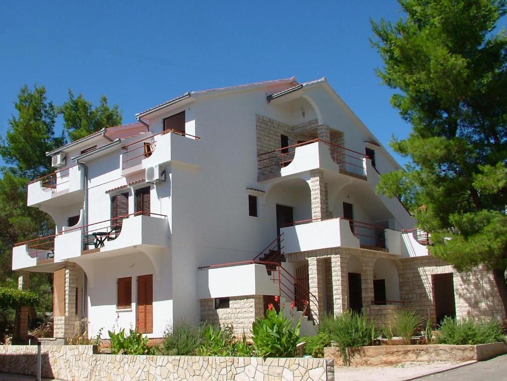 a large white building with balconies and trees at Apartments Pinus in Vrboska