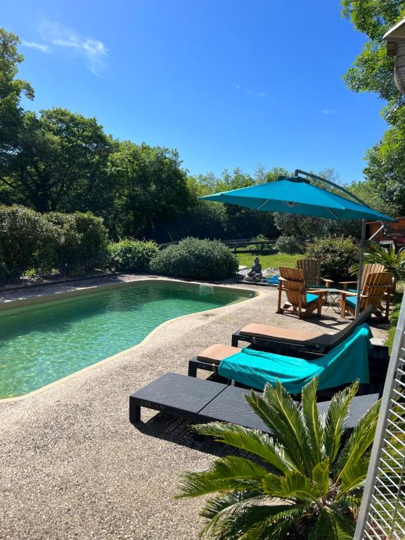 a swimming pool with chairs and an umbrella next to it at Chambre d hôte petit crussac in Mauvezin