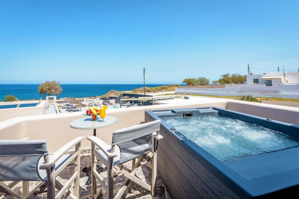 een zwembad met stoelen en een tafel en de oceaan bij En Plo Boutique Suites Oia Santorini in Oia