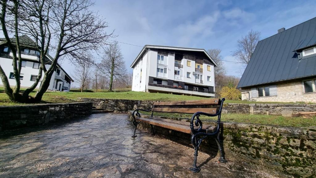 a park bench sitting next to a stone wall with a house at Apartman Filipčić in Plitvička Jezera