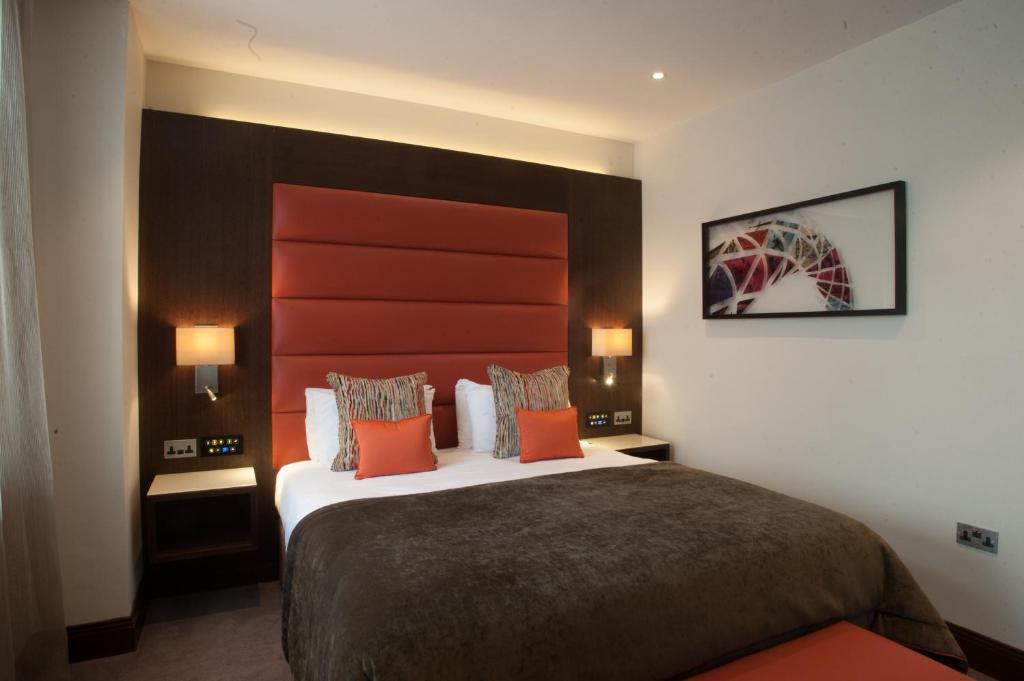 um quarto de hotel com uma cama grande com almofadas laranja em St George's Hotel - Wembley em Londres