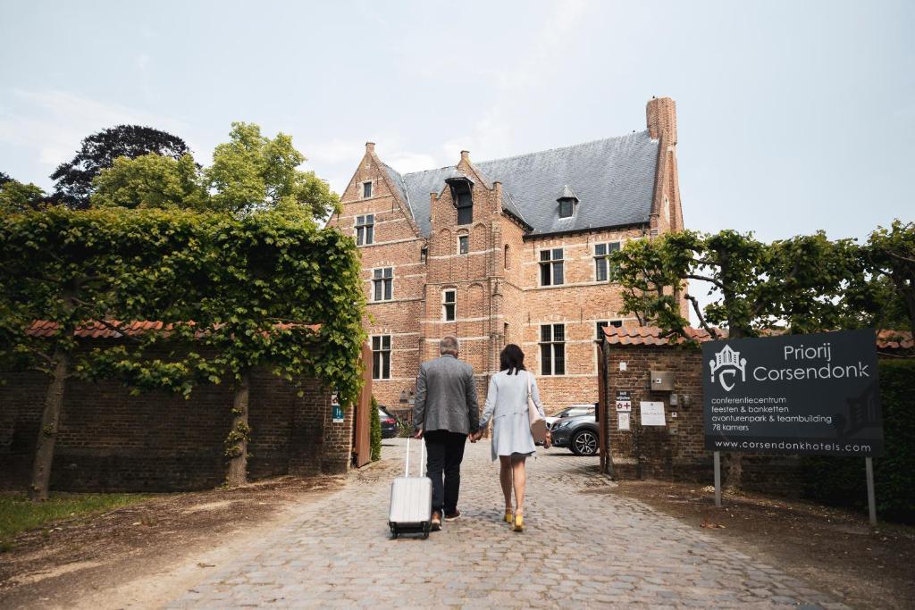 a man and woman walking down a street with luggage at Priorij Corsendonk in Oud-Turnhout