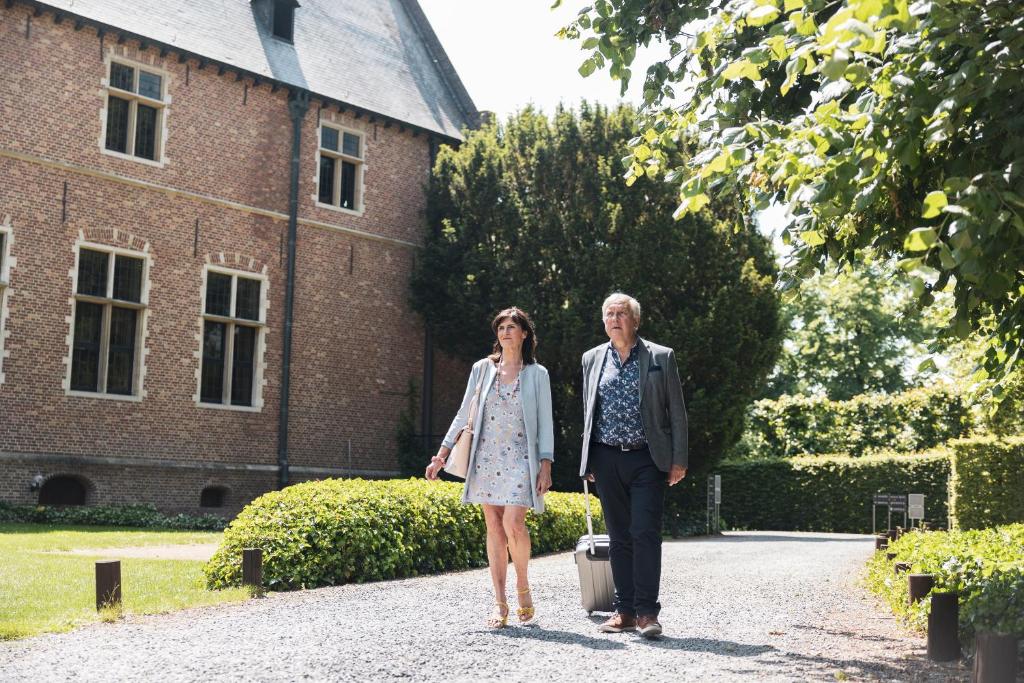 an older man and woman standing in front of a building with a suitcase at Priorij Corsendonk in Oud-Turnhout