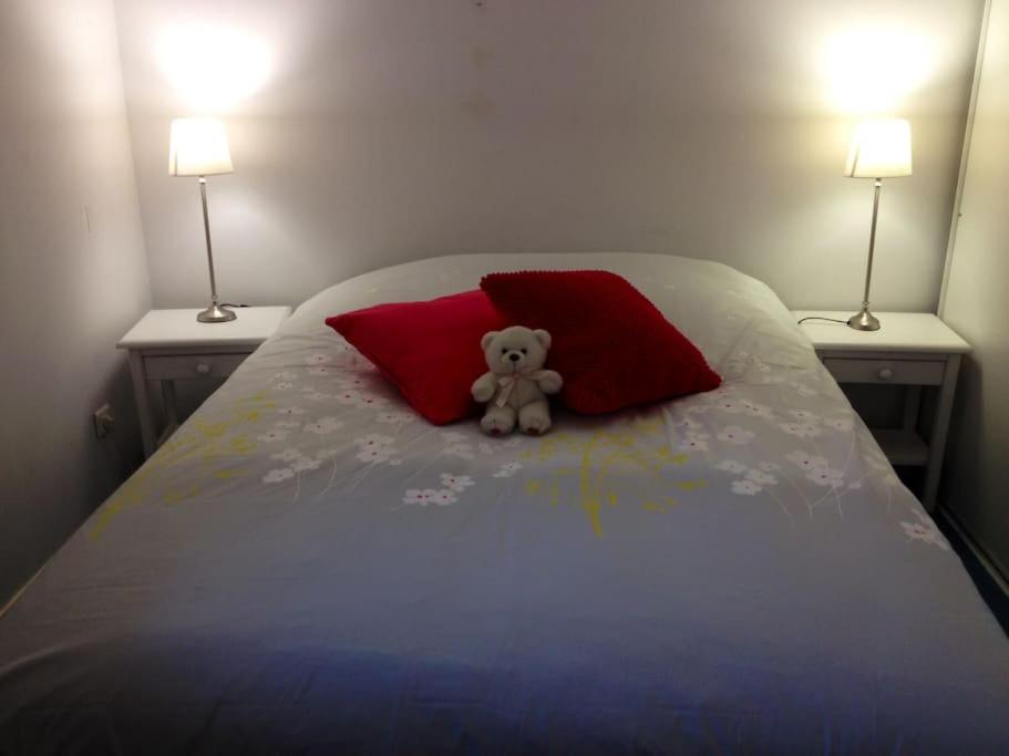 a teddy bear sitting on a bed with two red pillows at Loft, terrasse au soleil - Vue mer, à deux pas de tout in Wissant