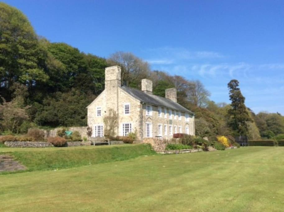 a large white house on a green field at Wolford Lodge Traditional home surrounded 150 private acres with Tennis court in Honiton