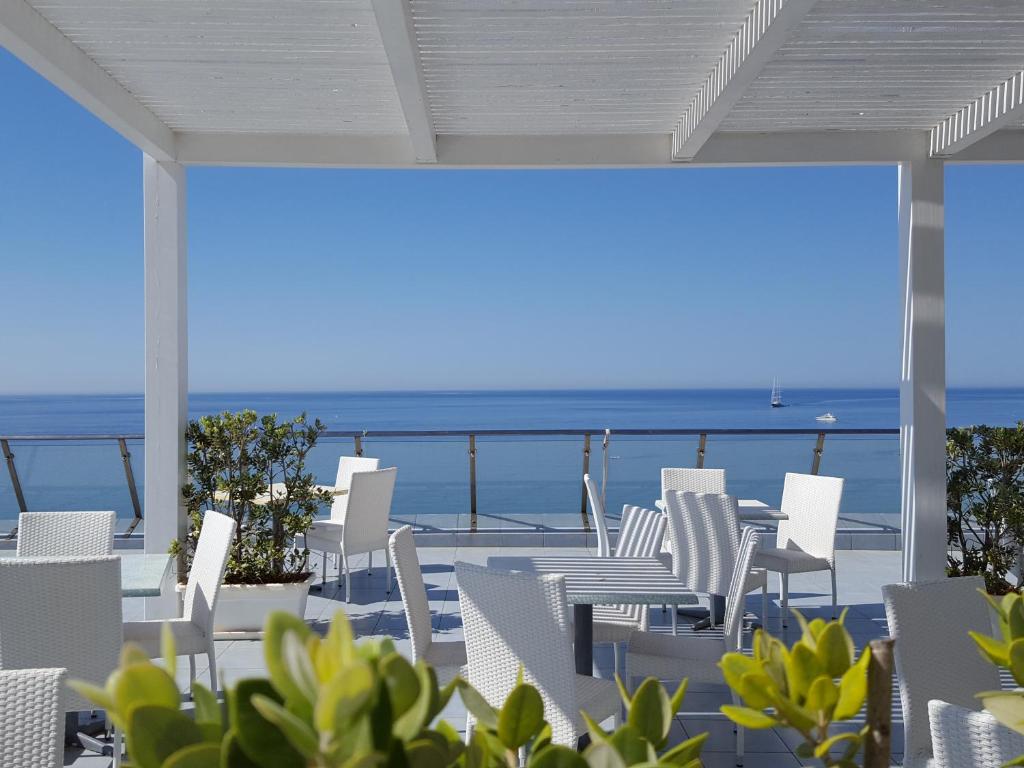 un patio con sillas blancas y vistas al océano en Hotel Admeto, en Marinella di Selinunte
