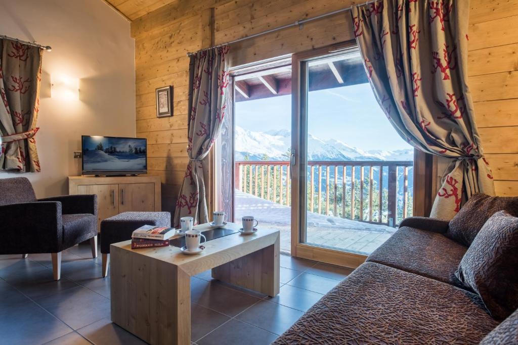a living room with a couch and a large window at CGH Résidences &amp; Spas Chalet Les Marmottons in La Rosière