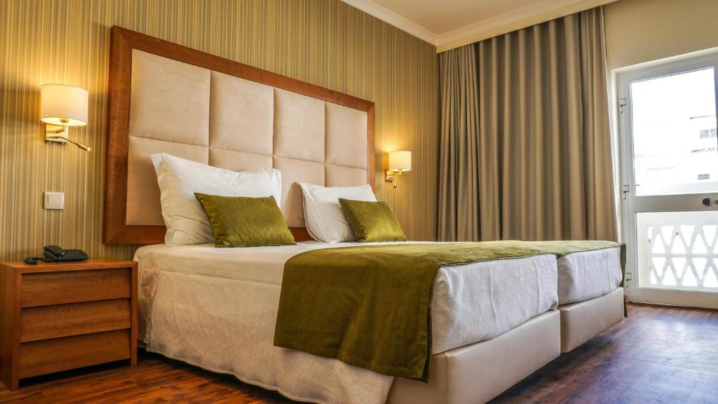 een slaapkamer met een groot bed met een groot hoofdeinde bij Hotel Baía De Monte Gordo in Monte Gordo