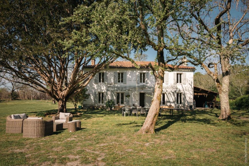 una casa bianca con degli alberi di fronte di Entre Chênes et Pins - Gîte de groupe 3 étoiles a Hostens