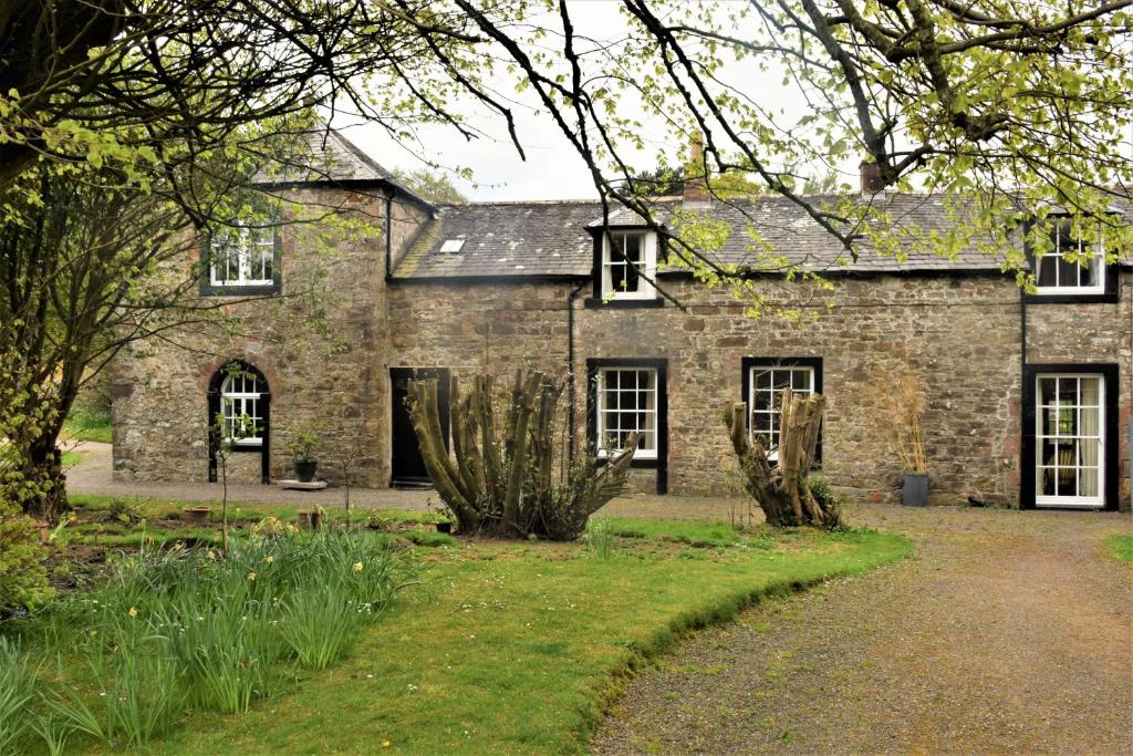 una antigua casa de piedra con un jardín delante de ella en The Stables, en Carsethorn