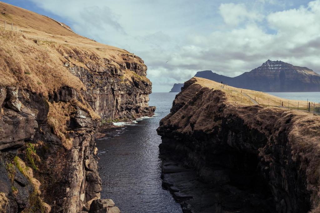 a river cutting through a rocky cliff next to the ocean at Cozy Cottage / 3BR / Hiking / Nature in Við Gjógv