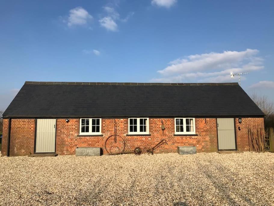 a brick house with a black roof in a field at The Cowshed in Salisbury