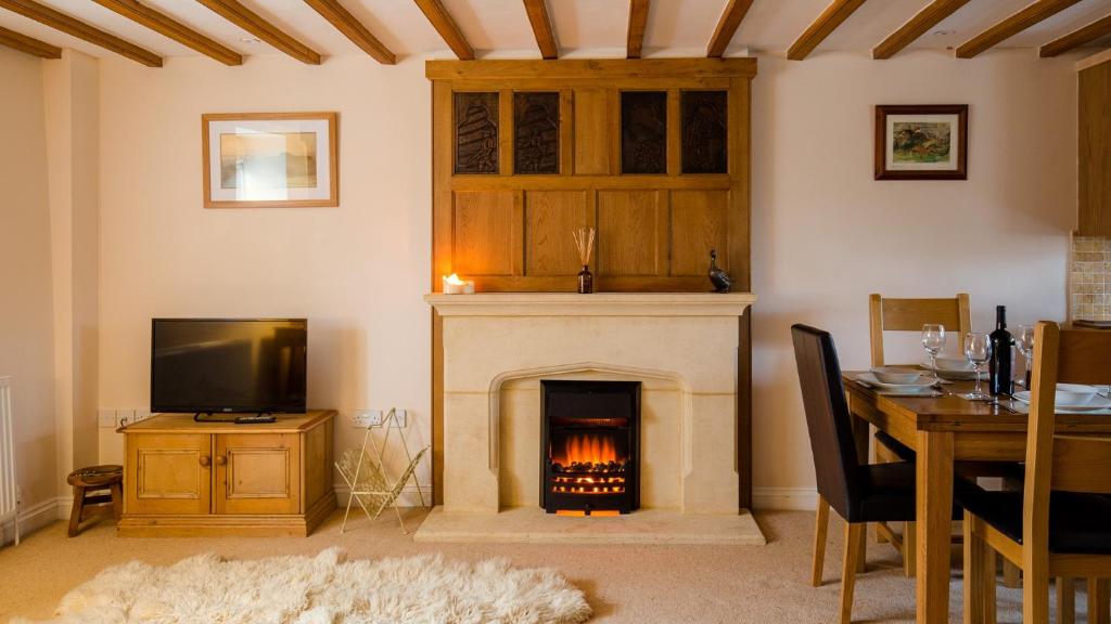 a living room with a fireplace with a table and a television at Old Mill Barn in Chipping Campden