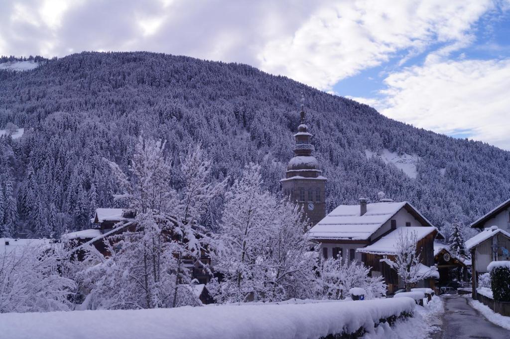 a snow covered mountain with a building and a tower at La petite Anfiane in Le Grand-Bornand