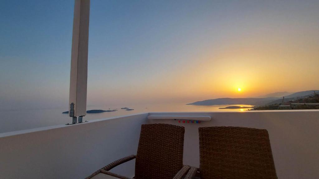 - deux chaises assises sur un balcon offrant une vue sur le coucher du soleil dans l'établissement Eolia luxury houses Andros, à Batsi