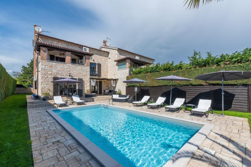 a pool with chairs and umbrellas in front of a house at Villa Olea Mare with Private Heated Pool in Buici