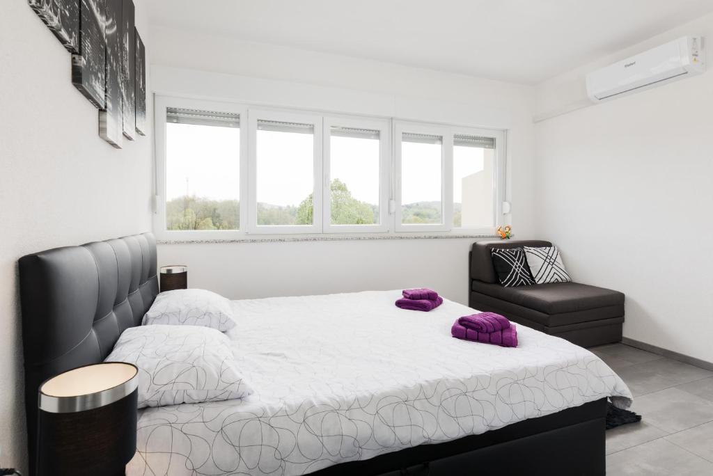 a white bedroom with a large bed and a chair at Studio apartman Sirius in Slunj