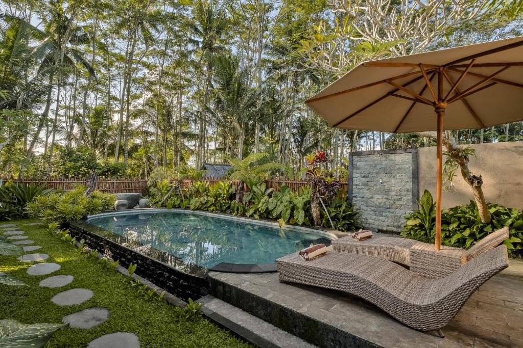 een zwembad met een parasol en twee stoelen en een tafel en een parasol bij Ratni Ubud Villa in Ubud