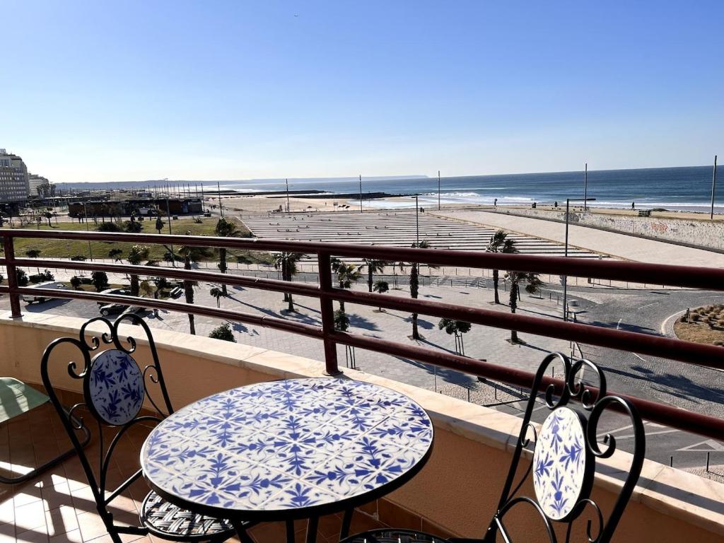 a balcony with a table and chairs and a view of the beach at O mar na frente de lux Caparica in Costa da Caparica