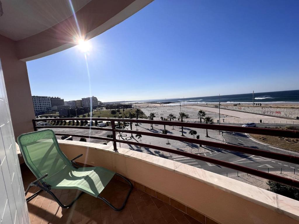 a green chair sitting on a balcony looking at the beach at O mar na frente de lux Caparica in Costa da Caparica