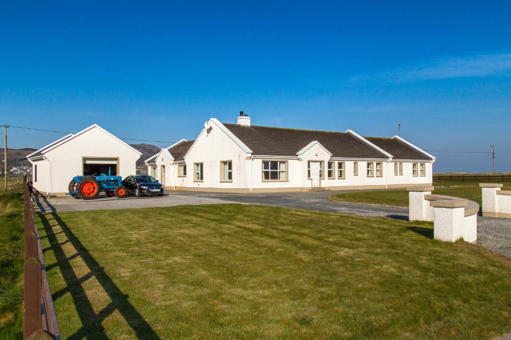 Uma casa branca com um tractor à frente. em Doherty's Country Accommodation em Ballyliffin