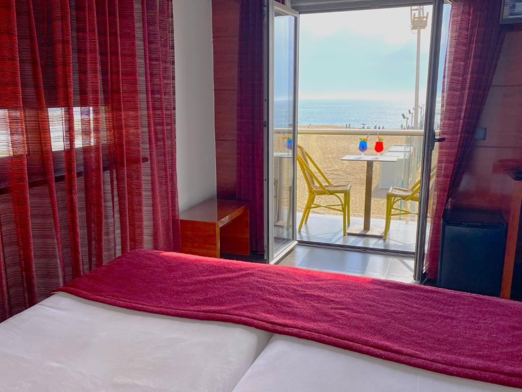a bedroom with a bed and a balcony with a table at Hotel Oceano in Nazaré