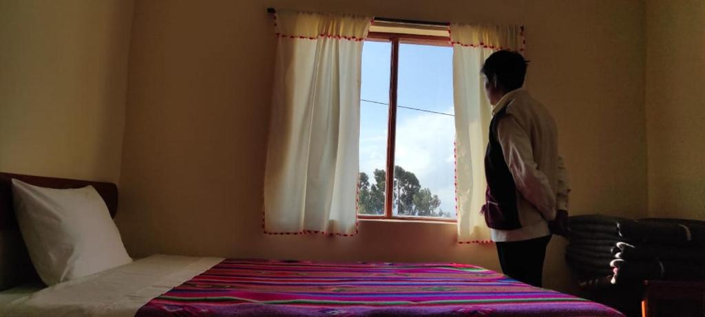 a man standing in a bedroom looking out the window at Lakeside Luquina in Puno