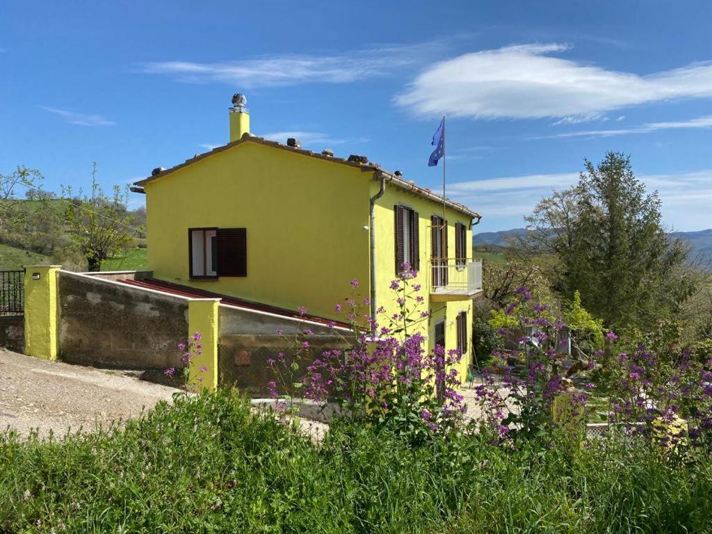 una casa amarilla con flores púrpuras delante de ella en La Villetta Marrucca en Grosseto