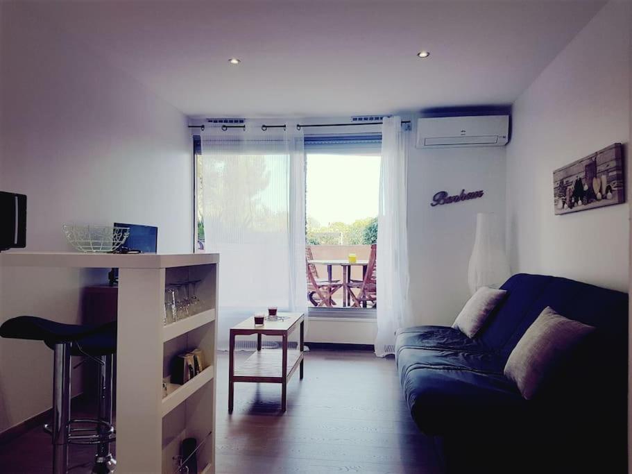 ein Wohnzimmer mit einem Sofa, einem Tisch und einem Fenster in der Unterkunft Logement cosy, calme, vue mer, sud France in La Seyne-sur-Mer
