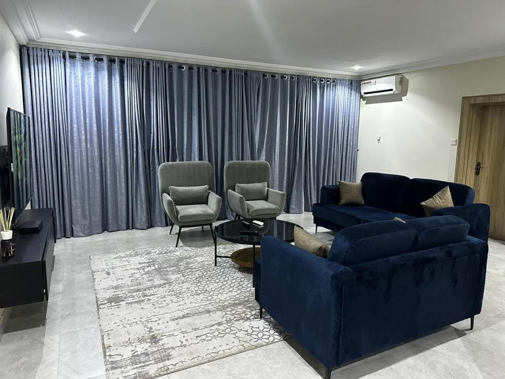 een woonkamer met een blauwe bank en 2 stoelen bij Modern City Center 3-Bed Apartment in Abuja
