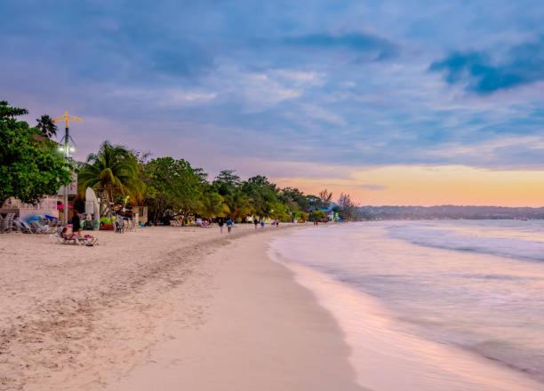 a beach with a group of people walking on the sand at Drifters@One Mile in Negril