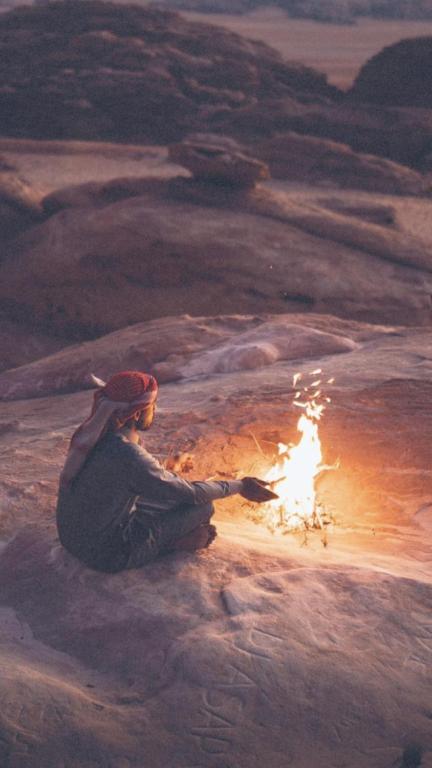 a person sitting on the ground with a fire at Wadirum Zeid Classic camp in Wadi Rum