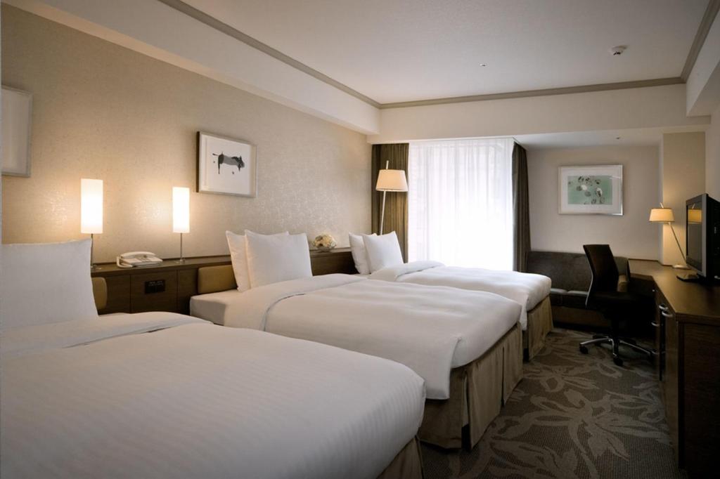a hotel room with three beds and a desk at Hotel Nikko Fukuoka in Fukuoka