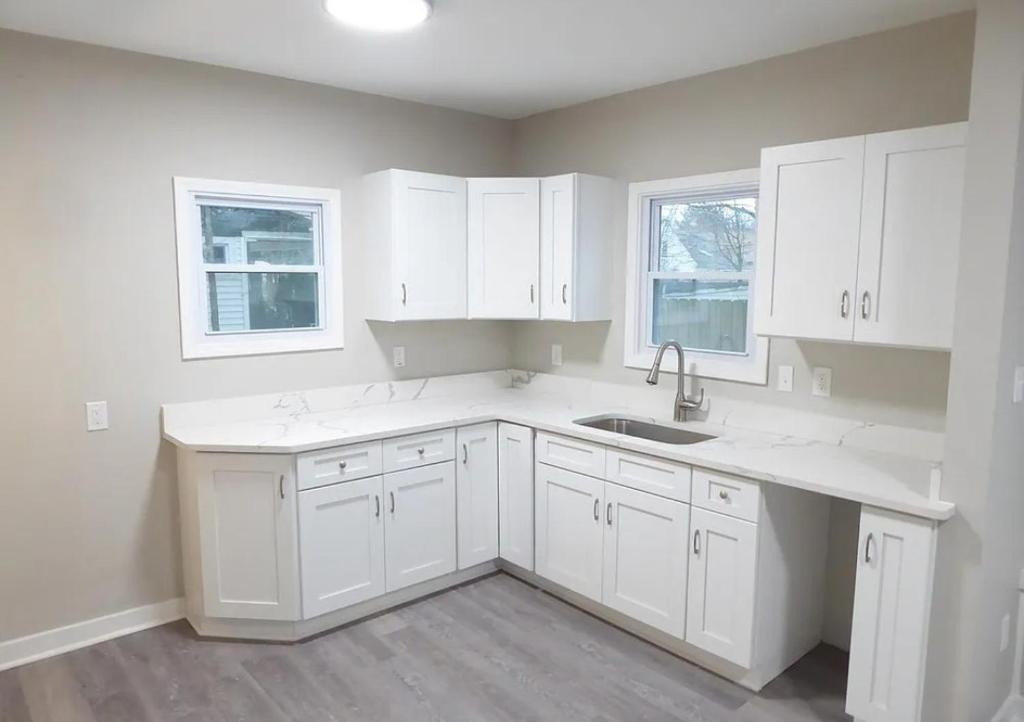 a kitchen with white cabinets and a sink and two windows at Spacious home in Missouri City