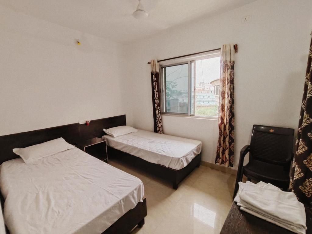 a bedroom with two beds and a window and a chair at Dwarka Home Stay in Bodh Gaya