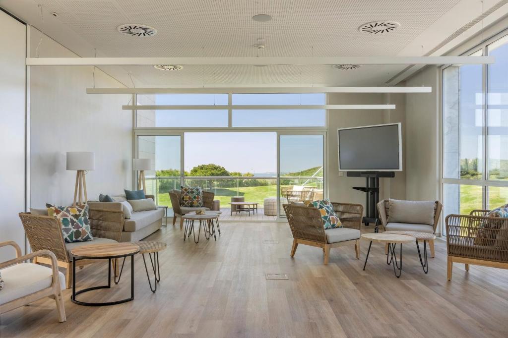 a living room with couches and a tv and windows at Crowne Plaza - Caparica Lisbon in Costa da Caparica