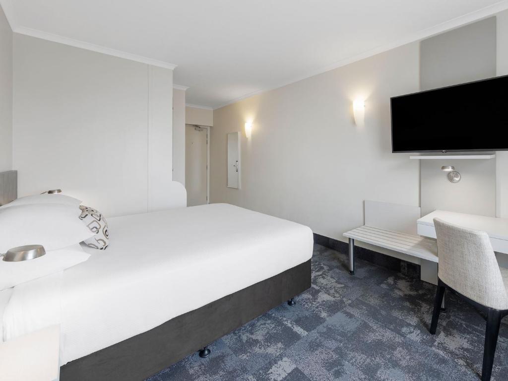 a bedroom with a bed and a desk and a tv at JetPark Auckland Airport Hotel in Auckland