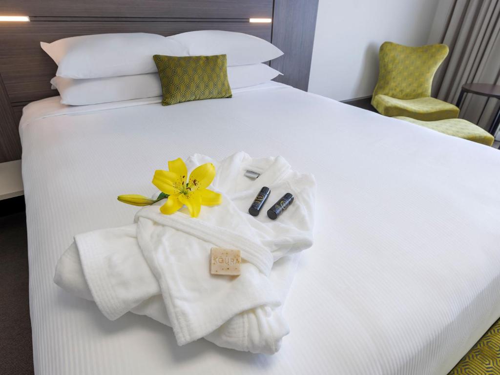 a hotel room with a white bed with towels and a flower on it at JetPark Auckland Airport Hotel in Auckland