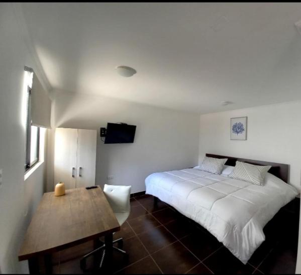 a bedroom with a white bed and a wooden table at Hotel Tabancura in Copiapó