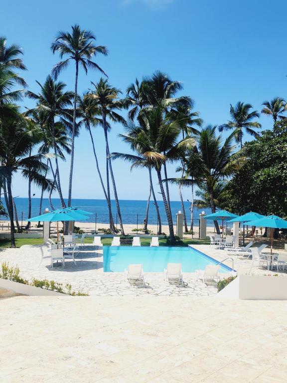 3 bedroom, front of the beach and pool في خوان دوليو: حمام سباحة على الشاطئ مع أشجار النخيل والمظلات الزرقاء