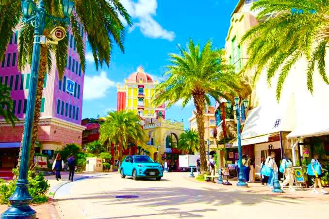 a blue car driving down a city street with palm trees at Luana Uakoko Resort 旧 EmiFull Resort in Chatan