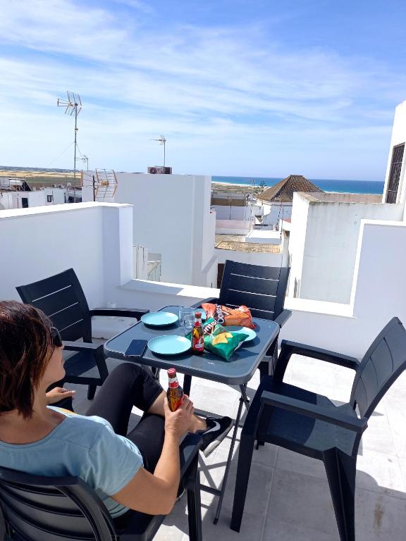 a woman sitting at a table on a balcony at Casa El Cuartel with private seaview rooftop in Conil de la Frontera