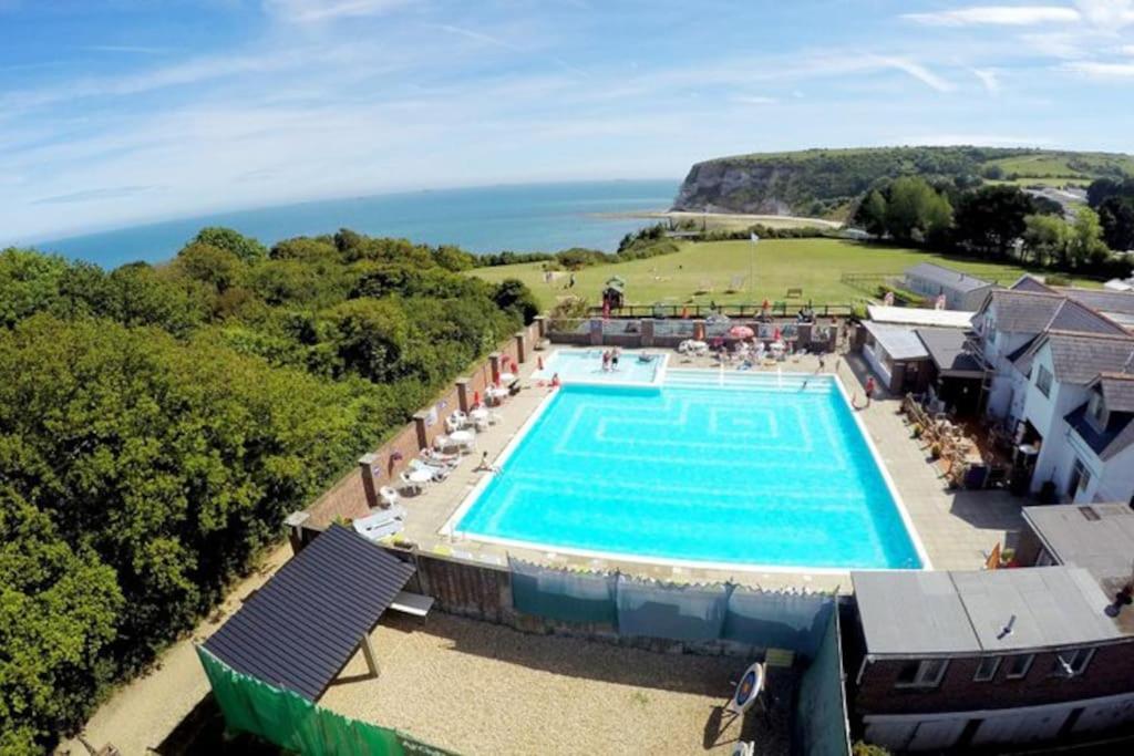 an overhead view of a swimming pool with the ocean in the background at Yarborough View 1 Whitecliff Bay Bembridge Isle of Wight in Bembridge