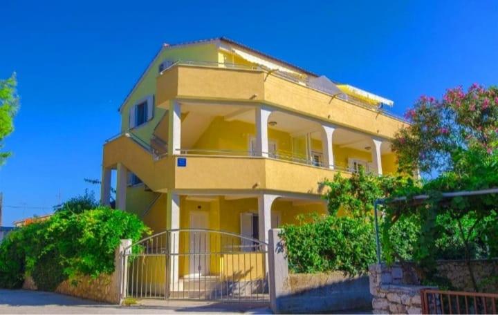 een groot geel huis met een hek ervoor bij Apartments Petrovic in Rogoznica