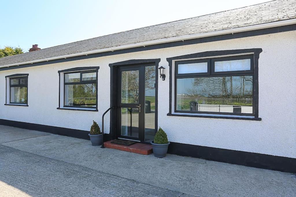 a white house with black windows and potted plants at Briglane Cottage in Kirkistown