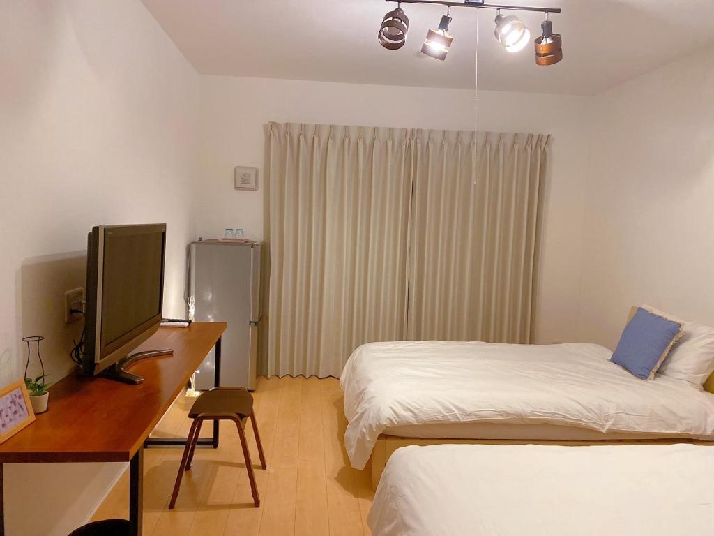 a bedroom with two beds and a desk with a television at Nakijin Resort Guest House in Nakijin
