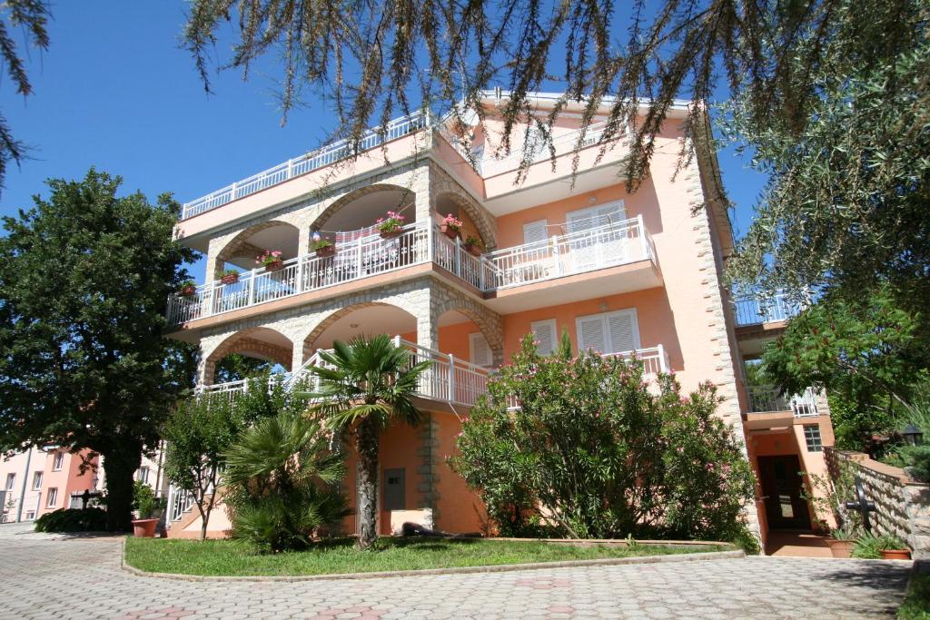 un grand bâtiment rose avec des balcons et des arbres dans l'établissement Apartments and Rooms Njivice, à Njivice